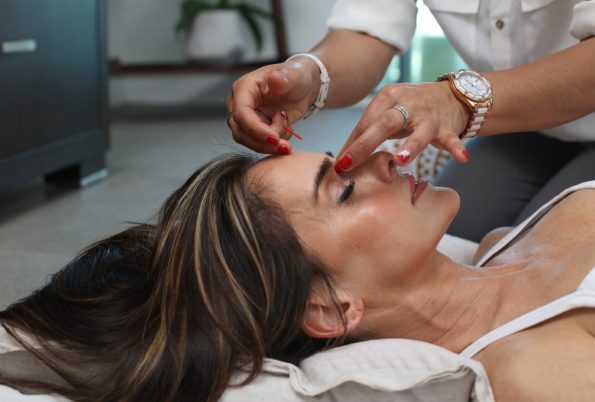 woman laying on a table while someone puts an acupuncture needle in her forehead.