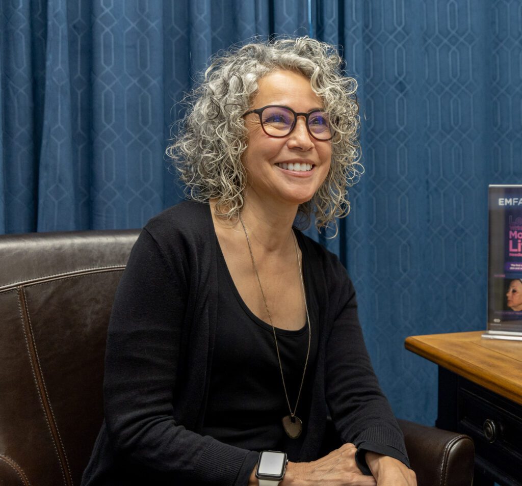 Mature woman with curly gray hair smiling in consultation room.